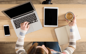 birdseye view of a teacher working at her desk with laptop, tablet, notebook and coffee.